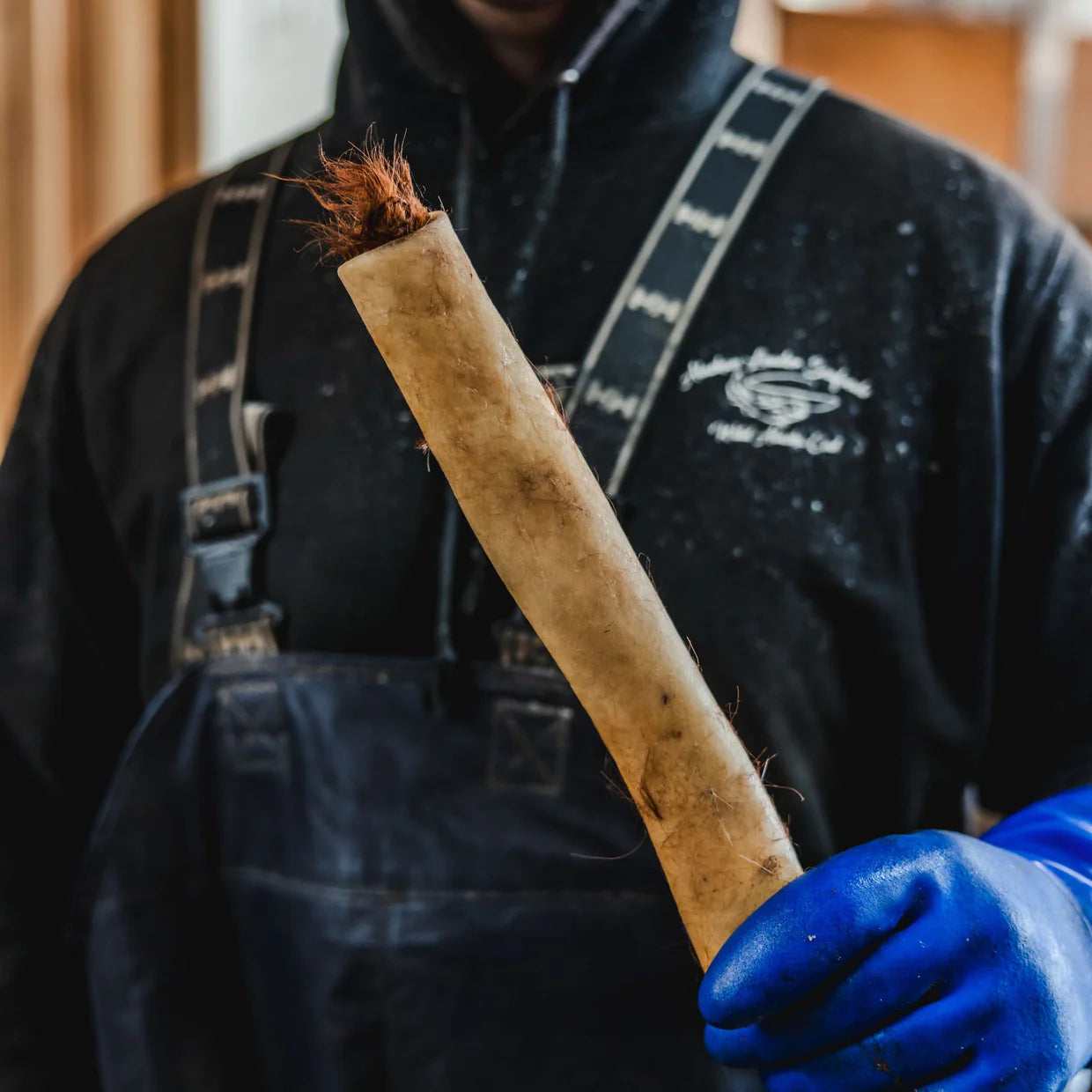 Person wearing a black jacket and blue gloves holding a long, cylindrical object with a natural finish.