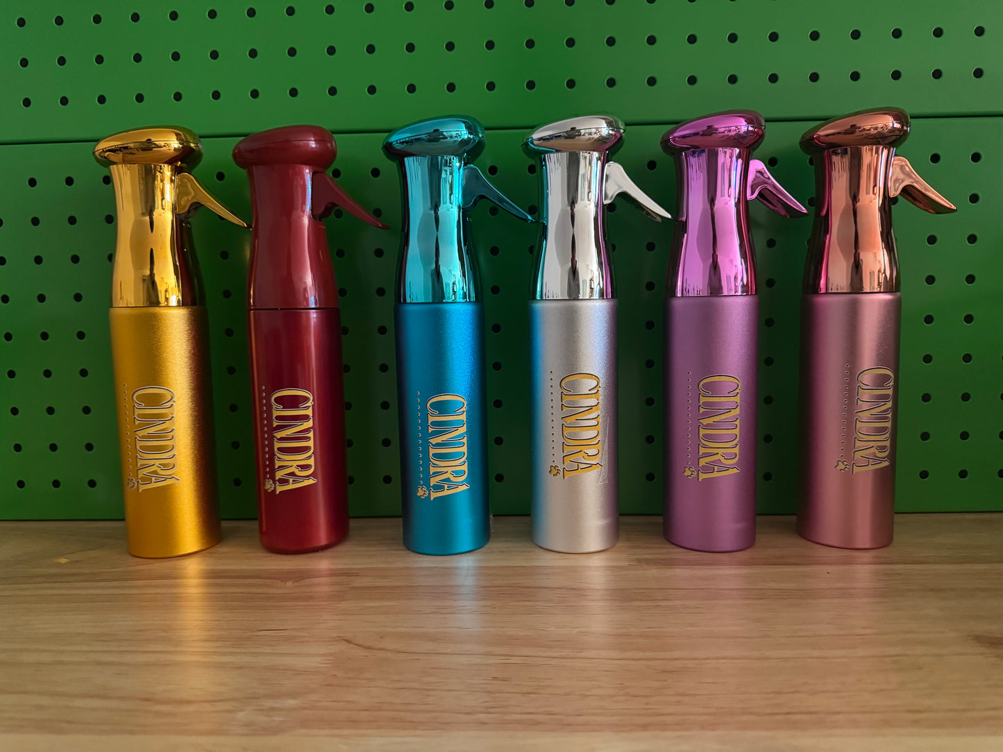 Cindra metallic grooming spray bottles in assorted colors lined up on a shelf.
