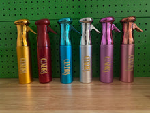 Load image into Gallery viewer, Cindra metallic grooming spray bottles in assorted colors lined up on a shelf.
