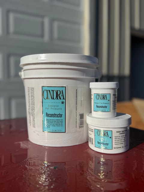Cindra Reconstructor product in a large bucket and two smaller containers on a red surface.